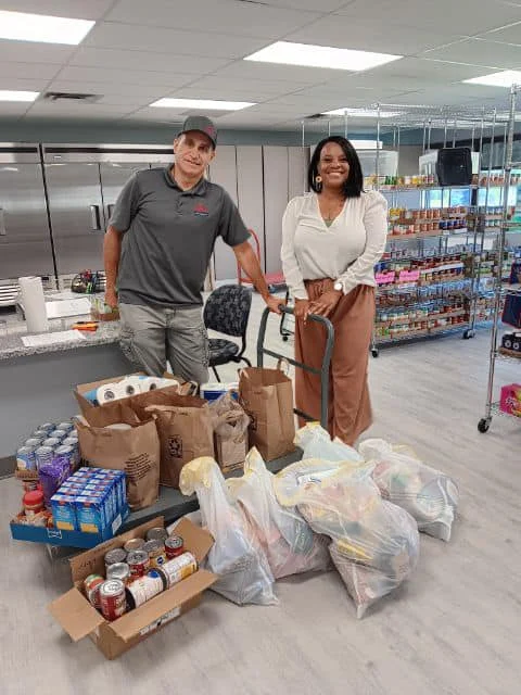A cart full of food ready for donation and two volunteers.