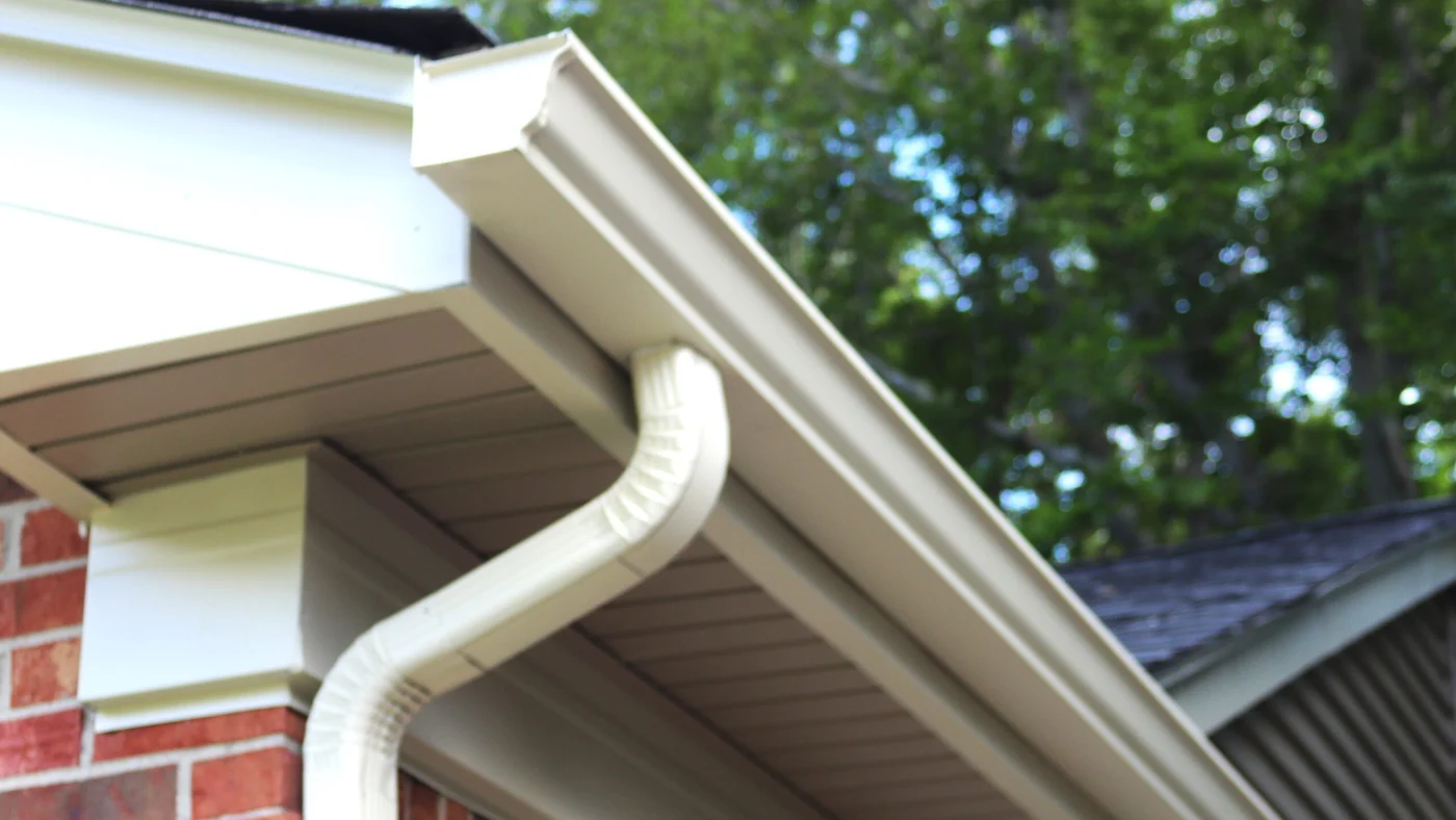 A tan seamless gutter with a downspout