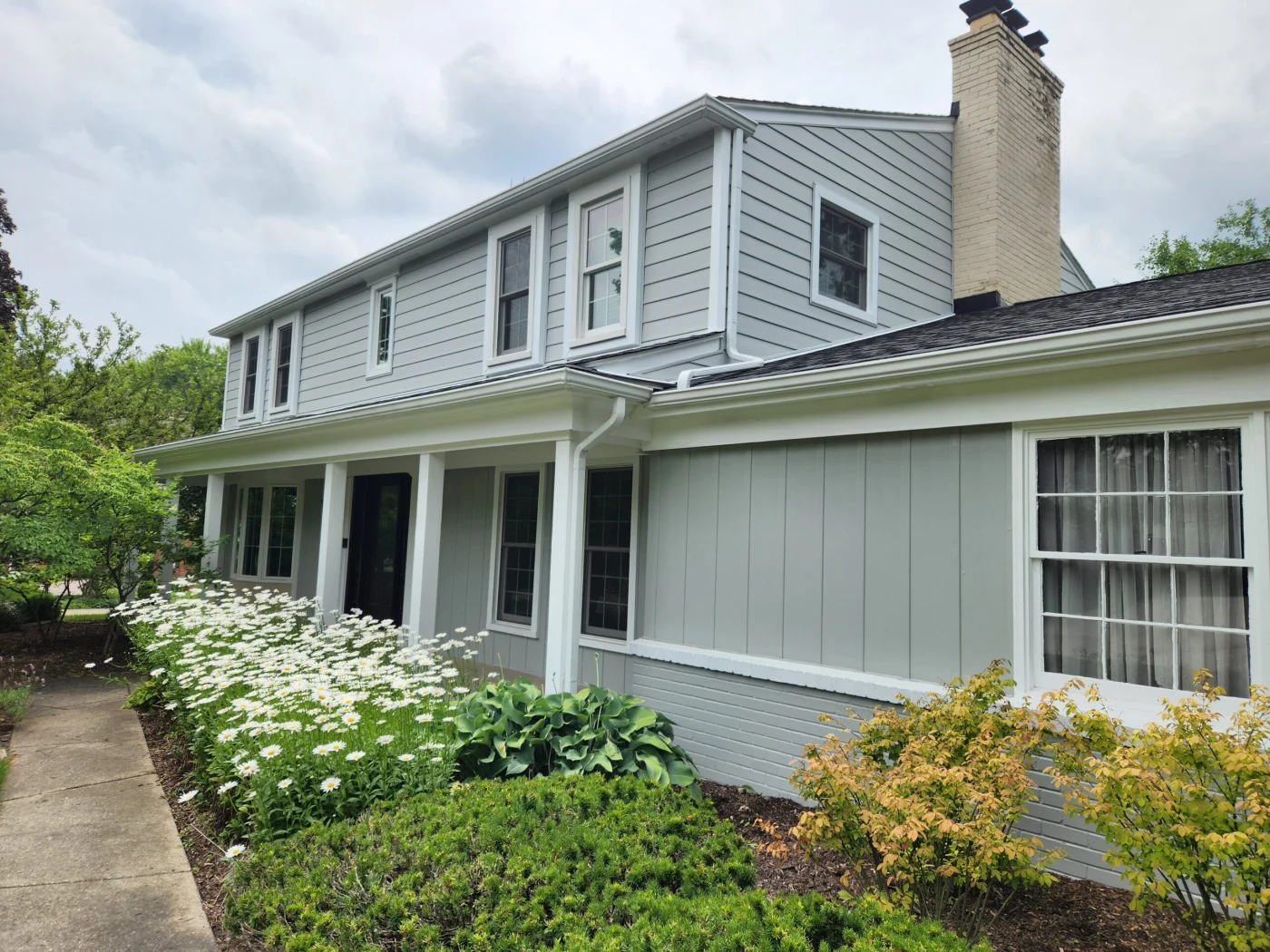 Large house with gray siding and daisies growing in garden