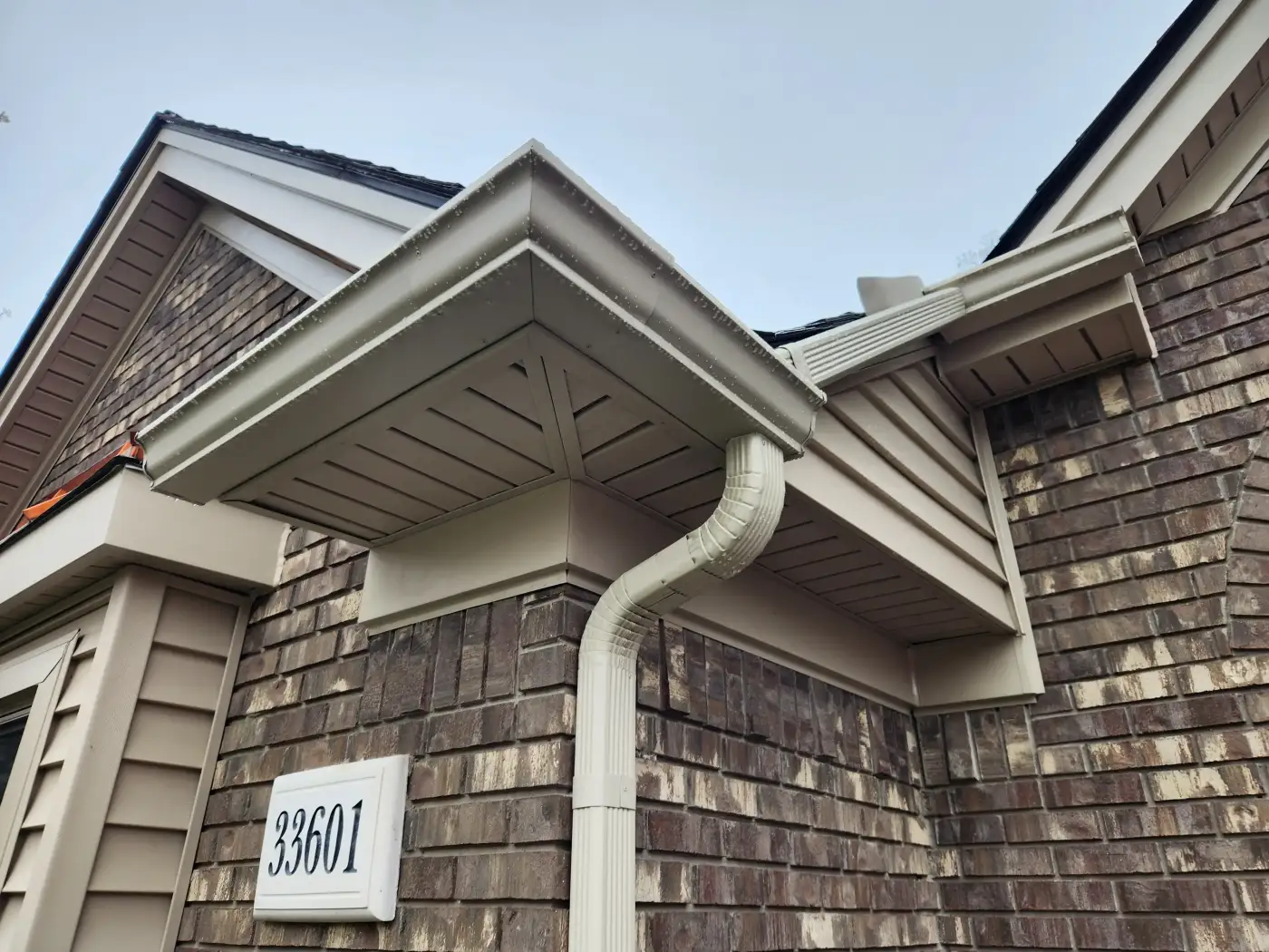 Corner of home with tan seamless gutters during rainstorm