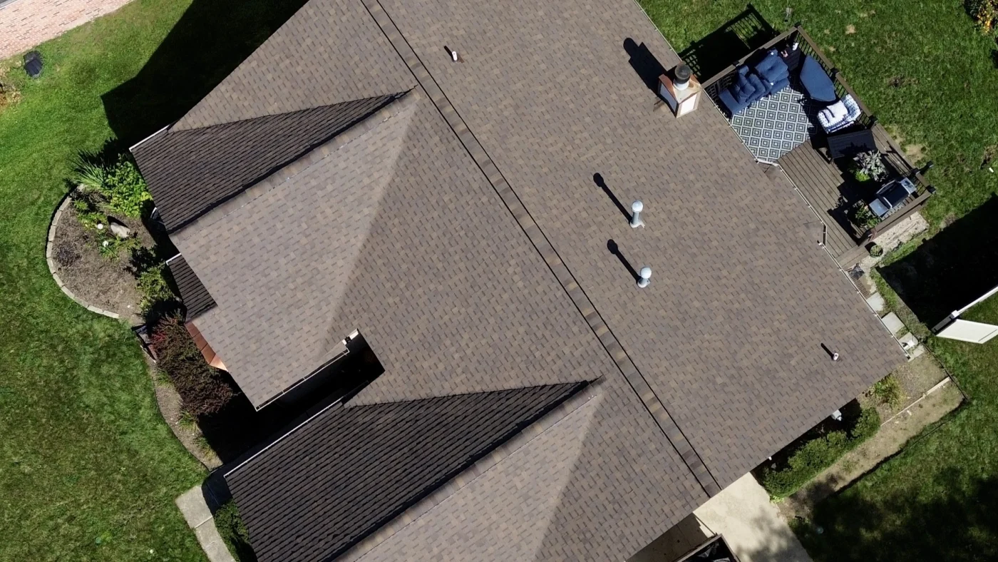 Bird’s eye view of home with brown shingle roof, brown backyard deck, and lush green backyard