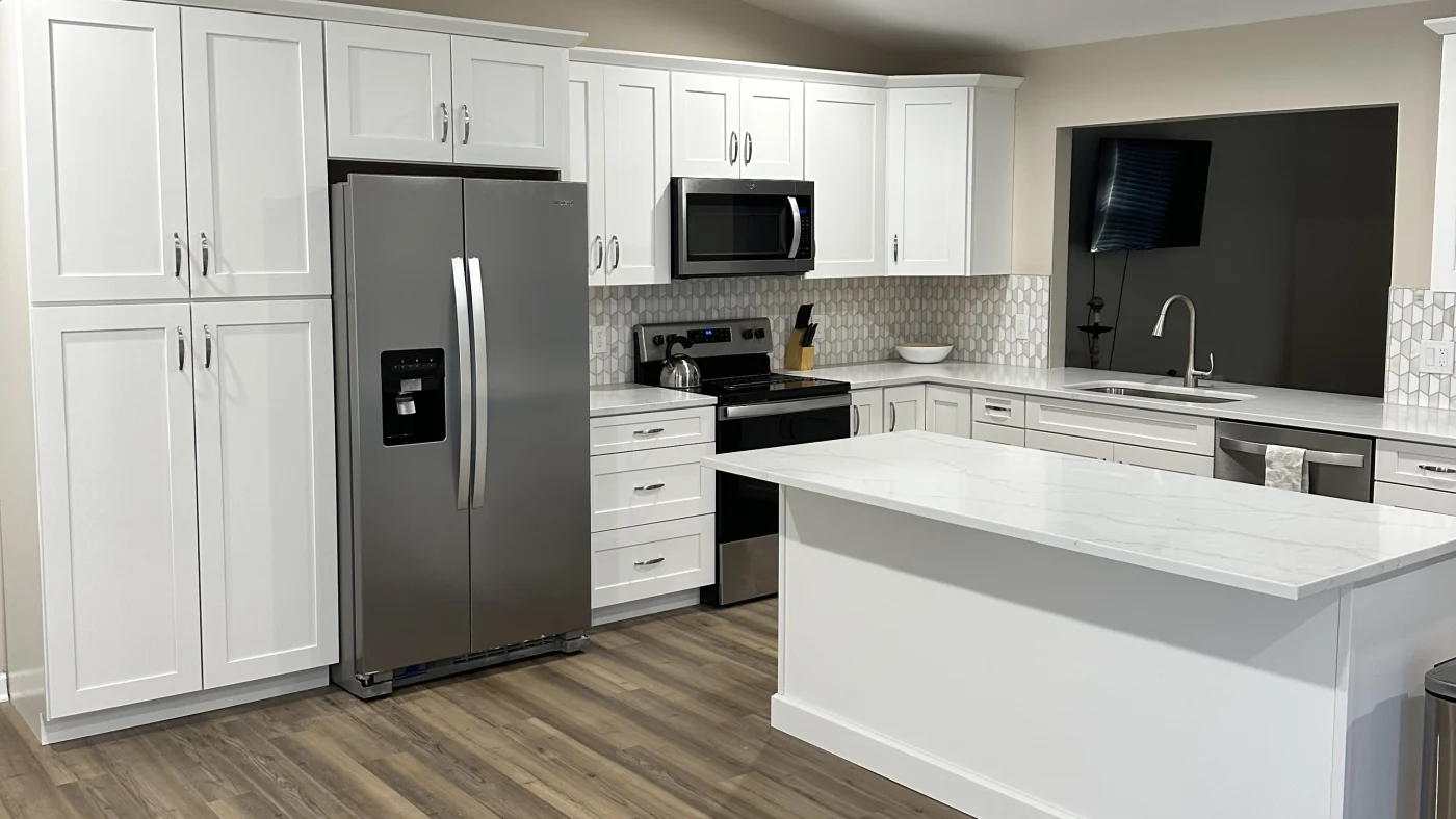 Beautiful kitchen remodel with white cabinets, patterned wallpaper, white island, white kitchen countertops, silver refrigerator, microwave, and stove