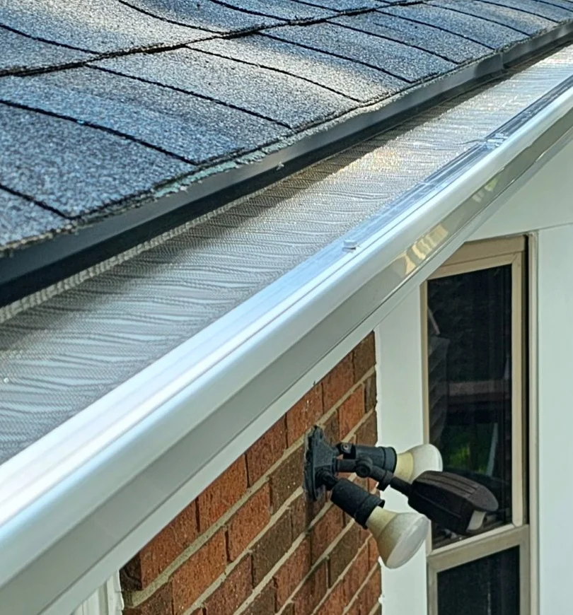 Gutter guard on the gutters of a brick house with an asphalt shingle roof.