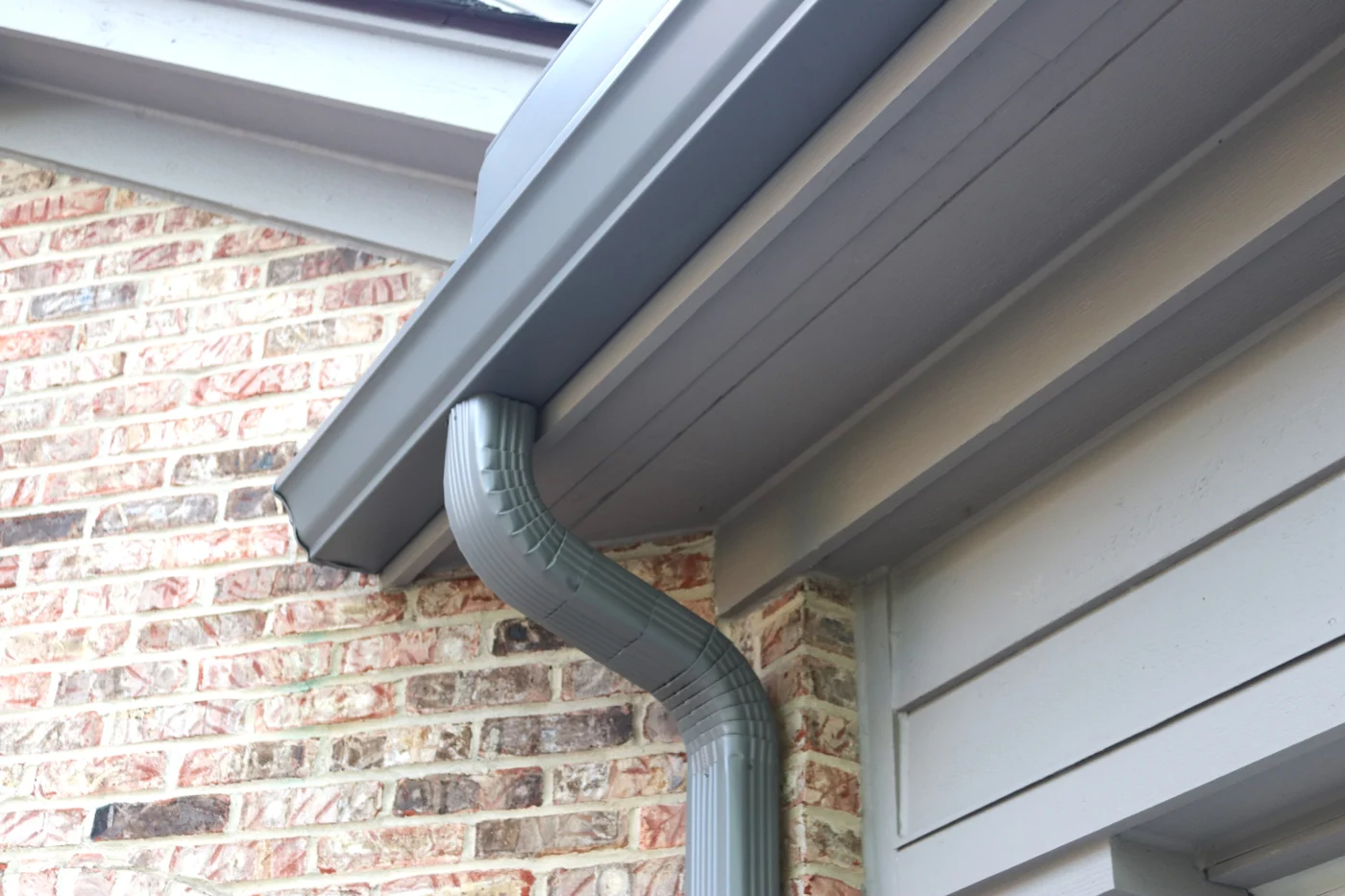 Gray seamless gutters and a downspout on a brick house.