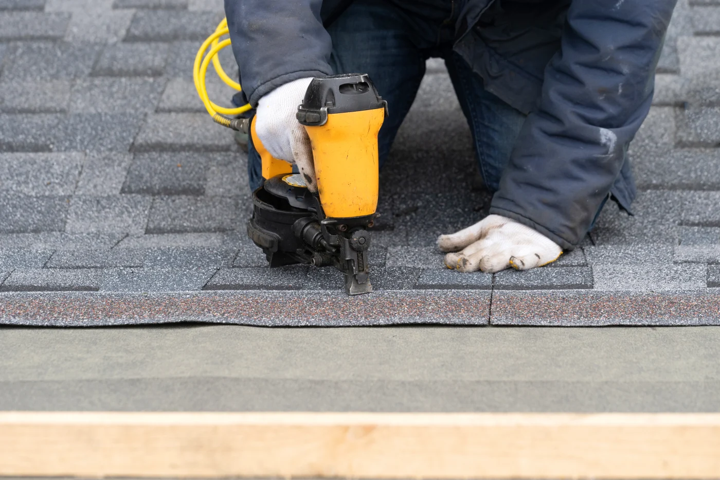 A roofer nailing new shingles on a roof during a residential roof replacement.