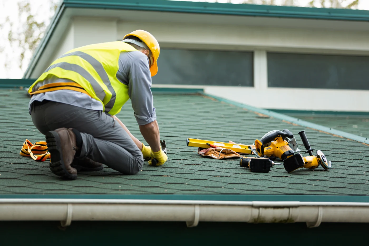 A roofer in safety equipment is making repairs to an asphalt shingle roof.