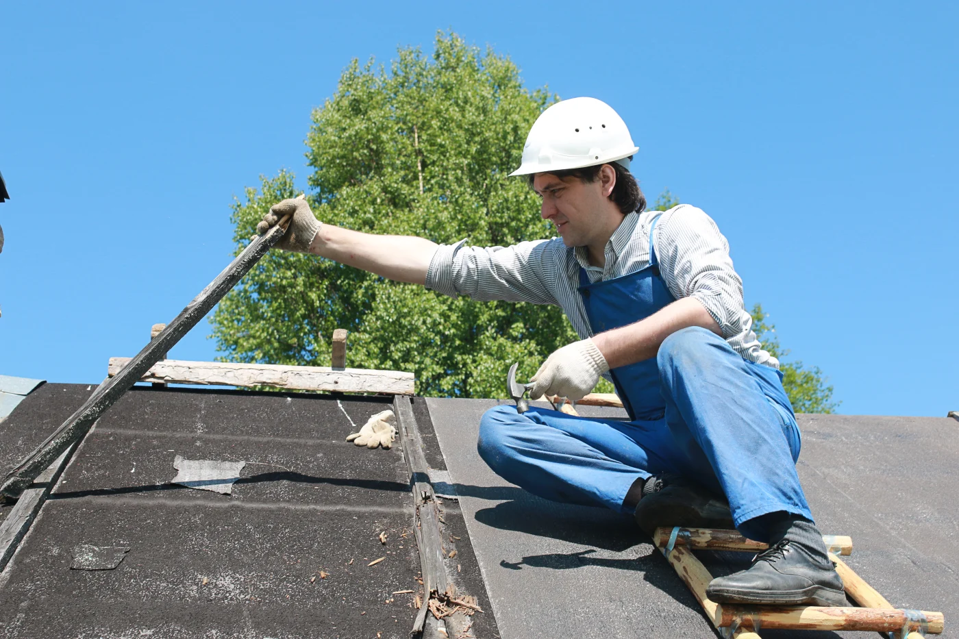A roofer making repairs to an asphalt shingle roof after storm damage.