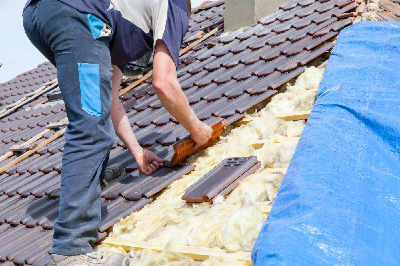 A roofer is installing new tiles on a roof during a roof replacement.