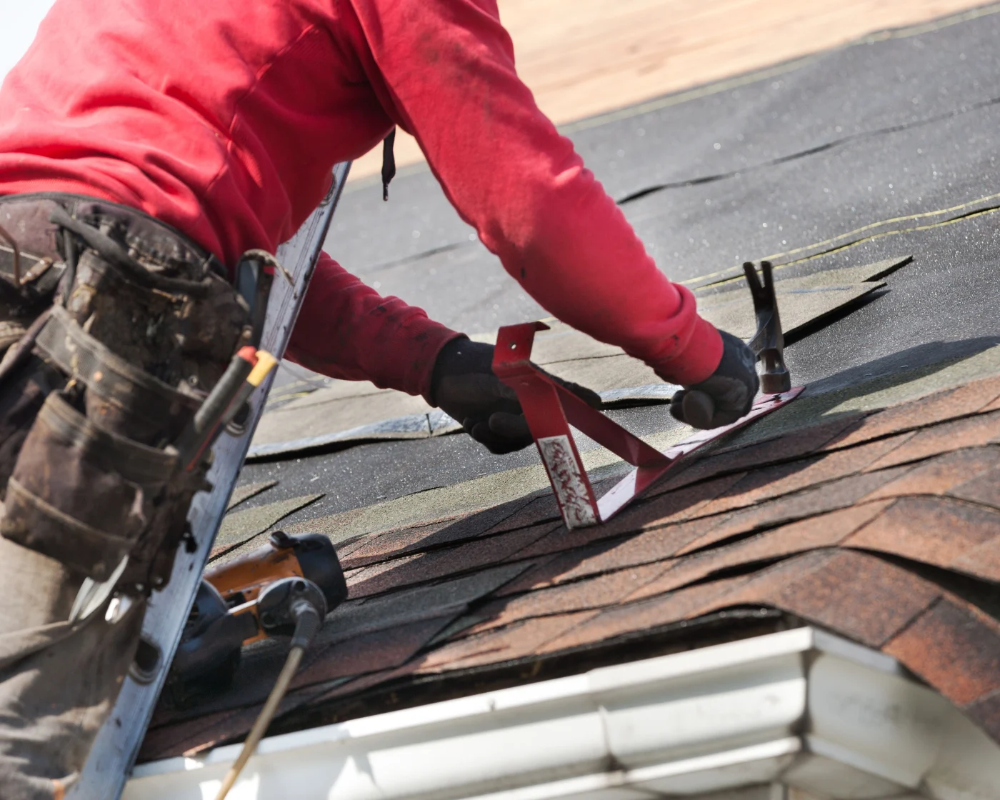 A roofer is hammering new shingles on a roof during a roof replacement.