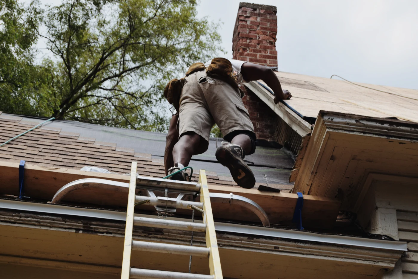 A roofer is climbing onto a roof to make storm damage repairs.