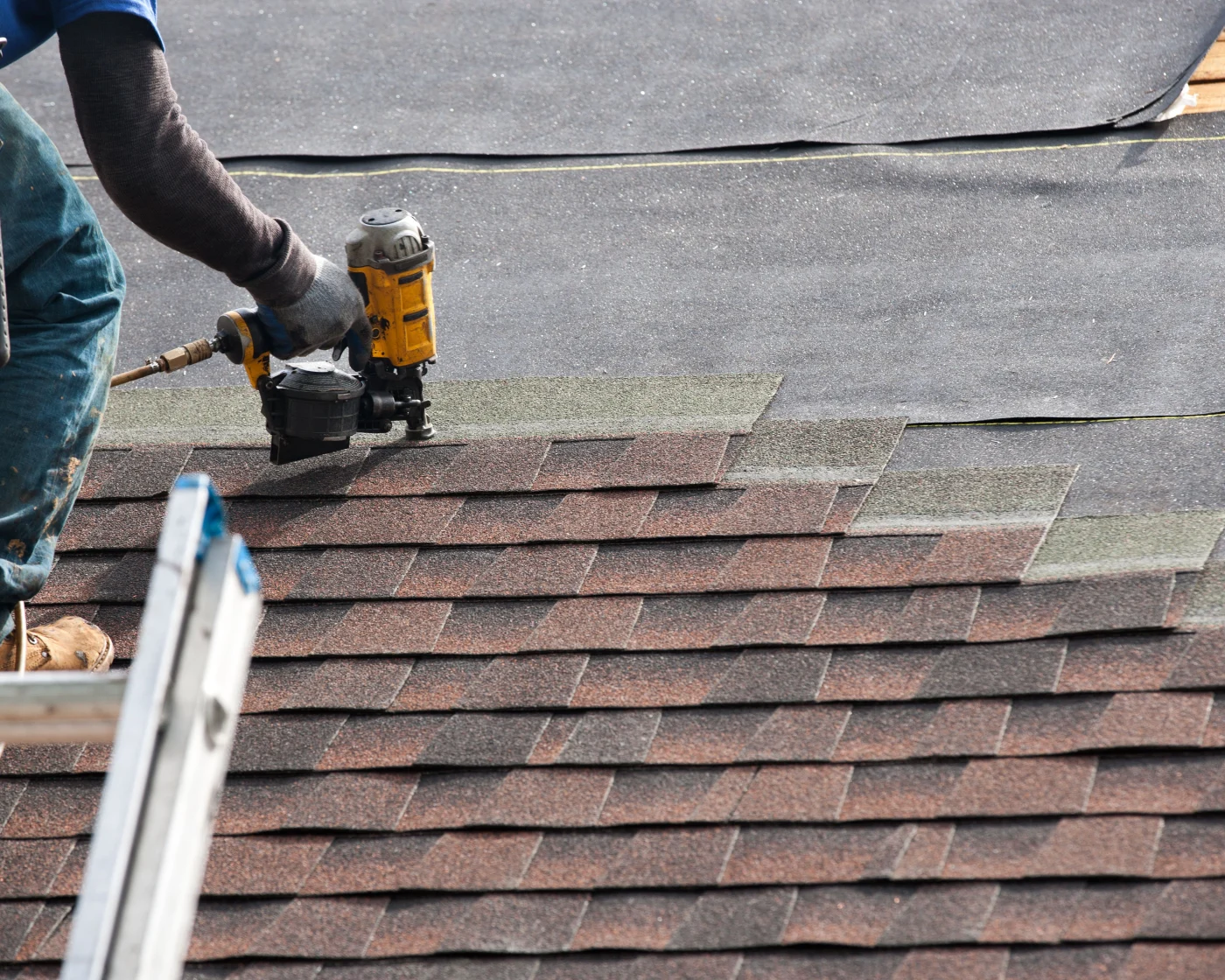 A roofer nailing asphalt shingles on a roof during a roof replacement.