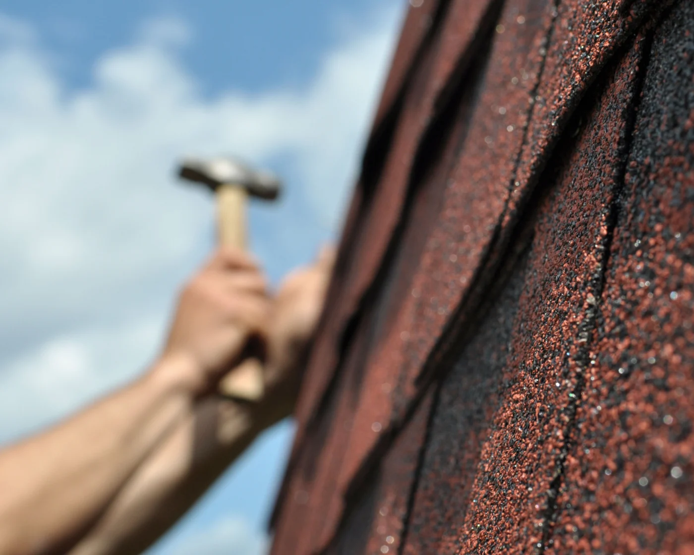 A roofer hammering new shingles onto a roof while repairing storm damage.