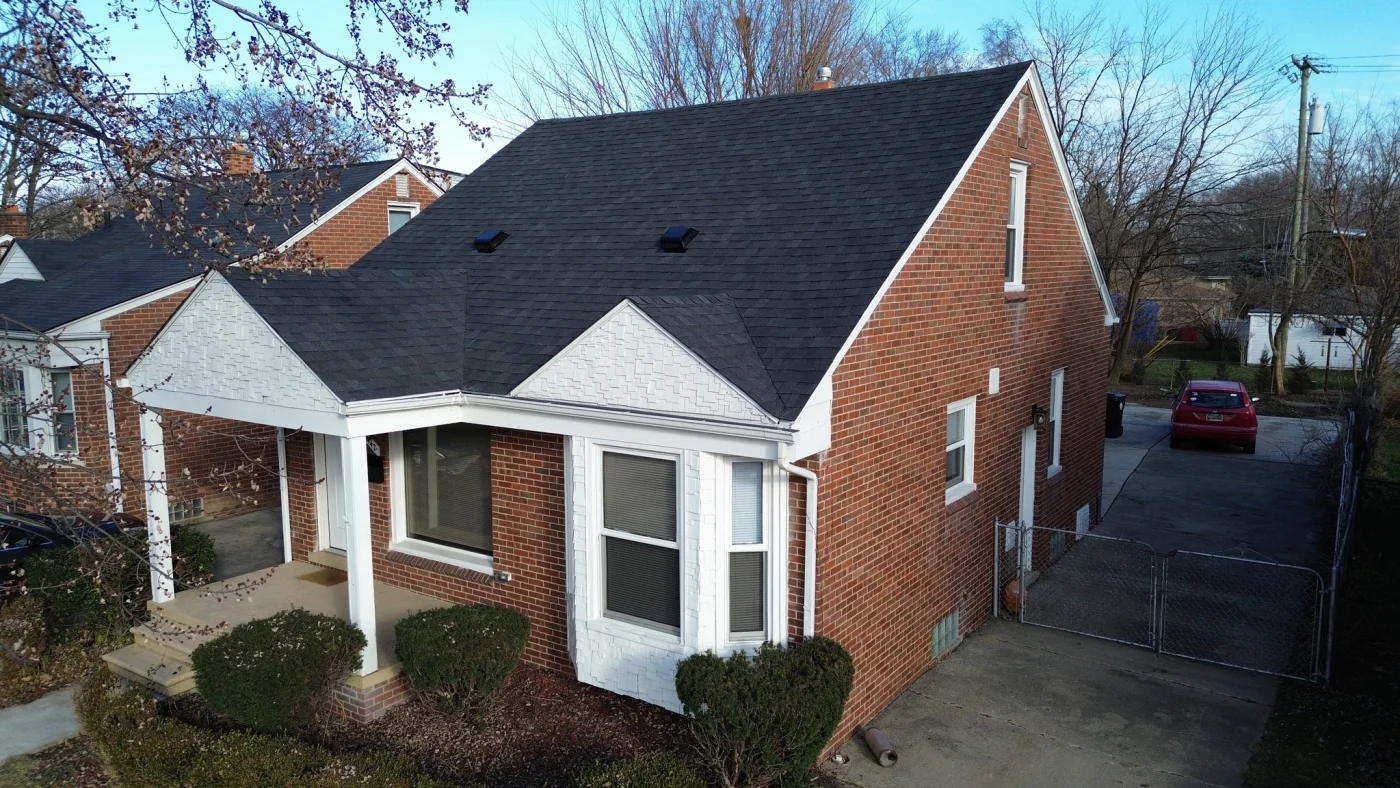 A black asphalt shingle roof on a brick house with white siding.