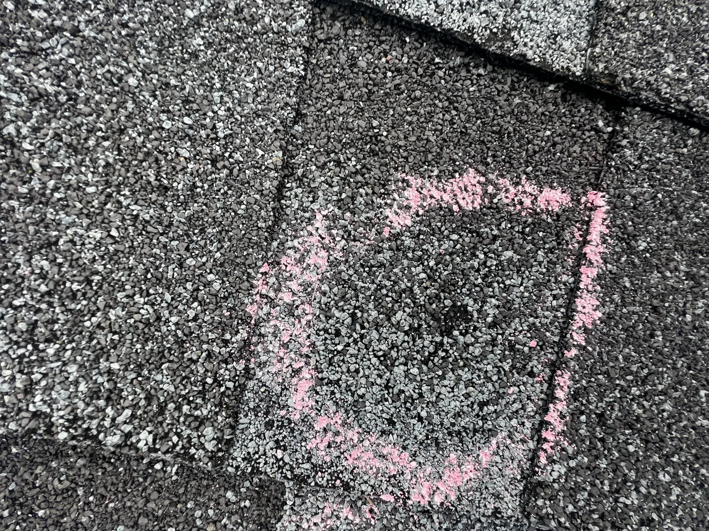 A close-up view of a hole in an asphalt shingle roof made by a storm circled in chalk.
