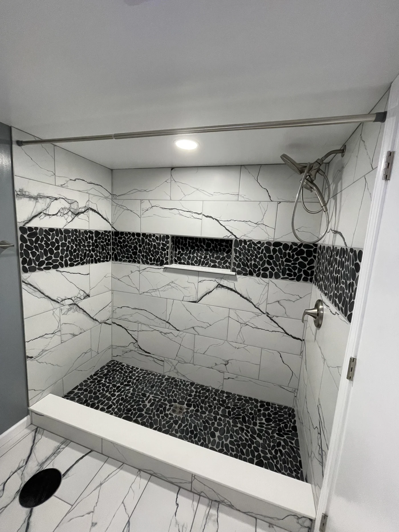 A walk-in shower with gray walls with a black stripe, a black base, built-in shelves, and silver fixtures.