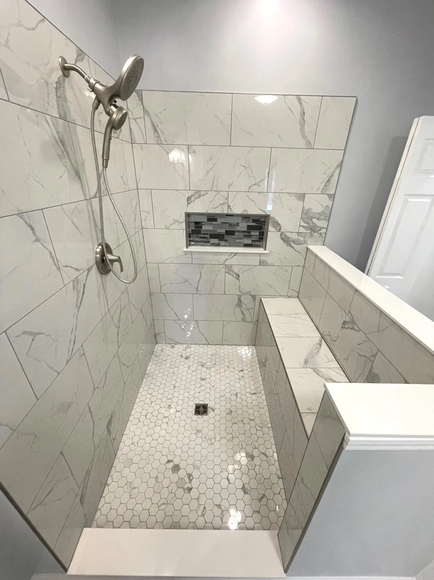 An off-white walk-in shower with a bench, built-in shelves, and silver fixtures.