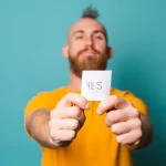A man holding a note that simply says “Yes” on it.