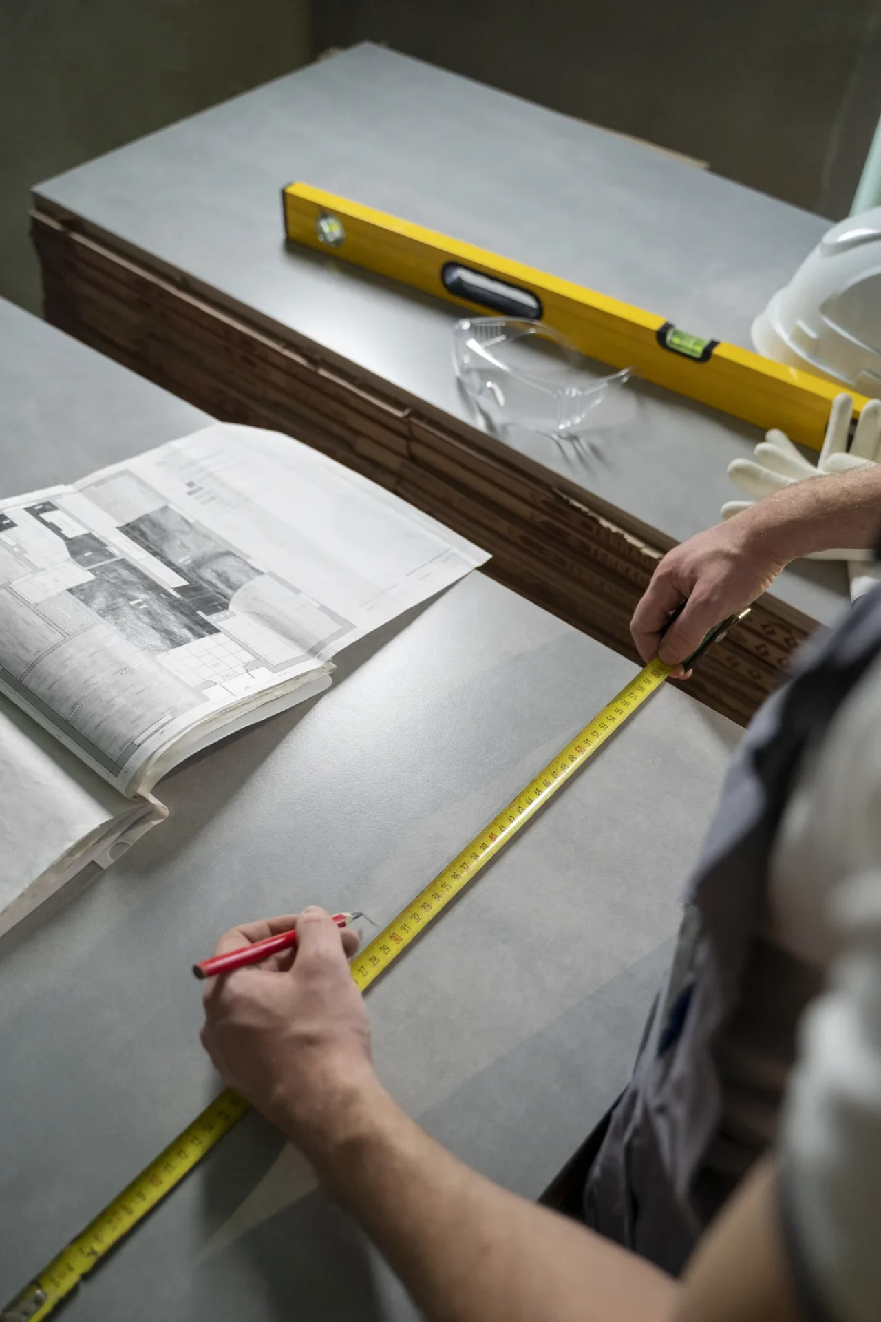 A Kroll Construction professional measures bathroom materials beside project plans, a level, safety glasses and installation supplies for a Canton, MI one-day bath update.