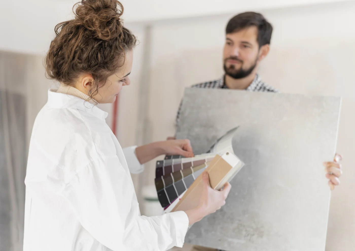 A homeowner reviews bathroom finish samples with a Kroll Construction representative holding a large tile panel during an in-home design consultation in Livonia, MI.