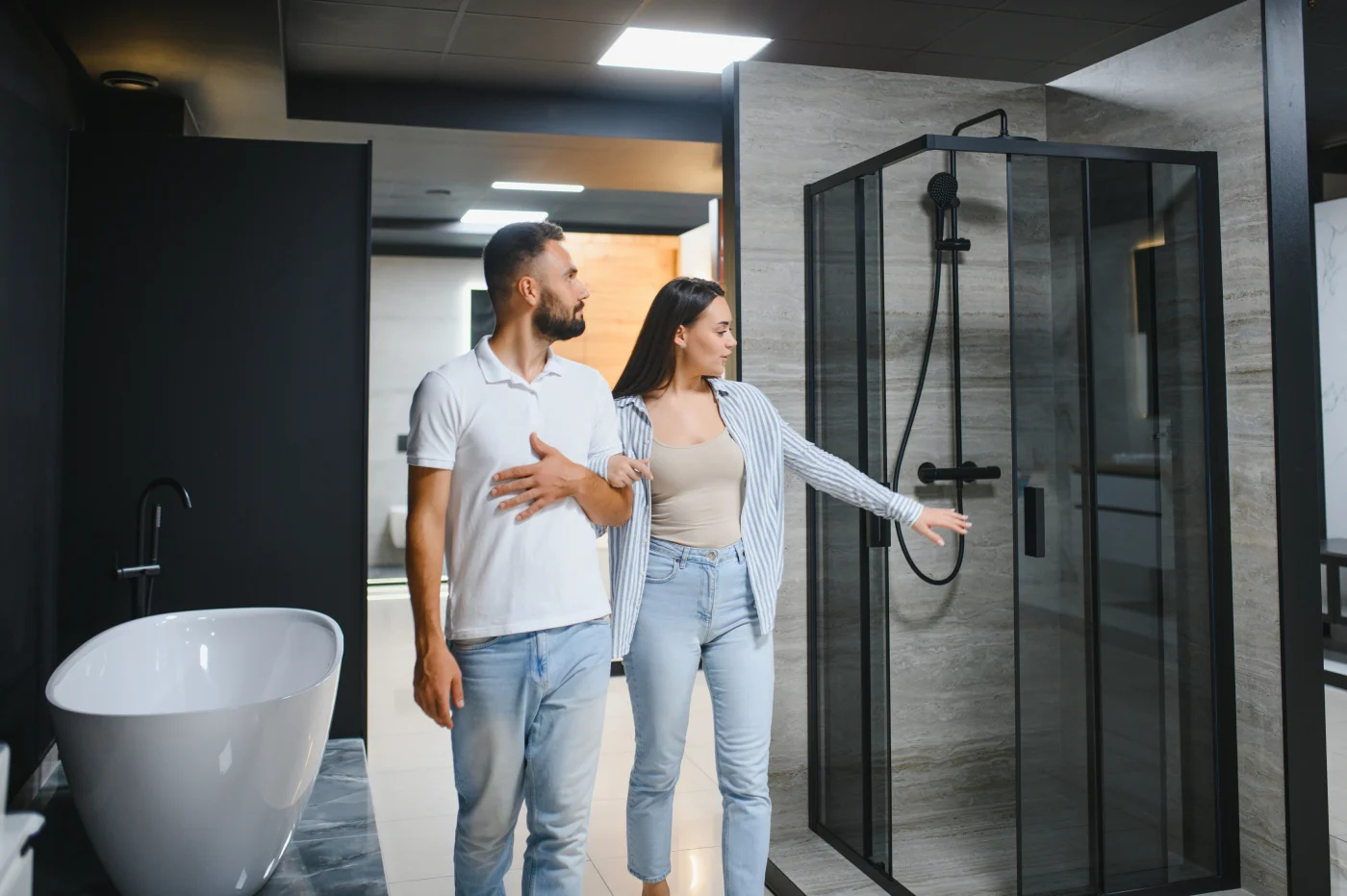 A couple compares a black-framed walk-in shower and a freestanding bathtub while choosing a new shower setup for a Livonia, MI bathroom remodel.
